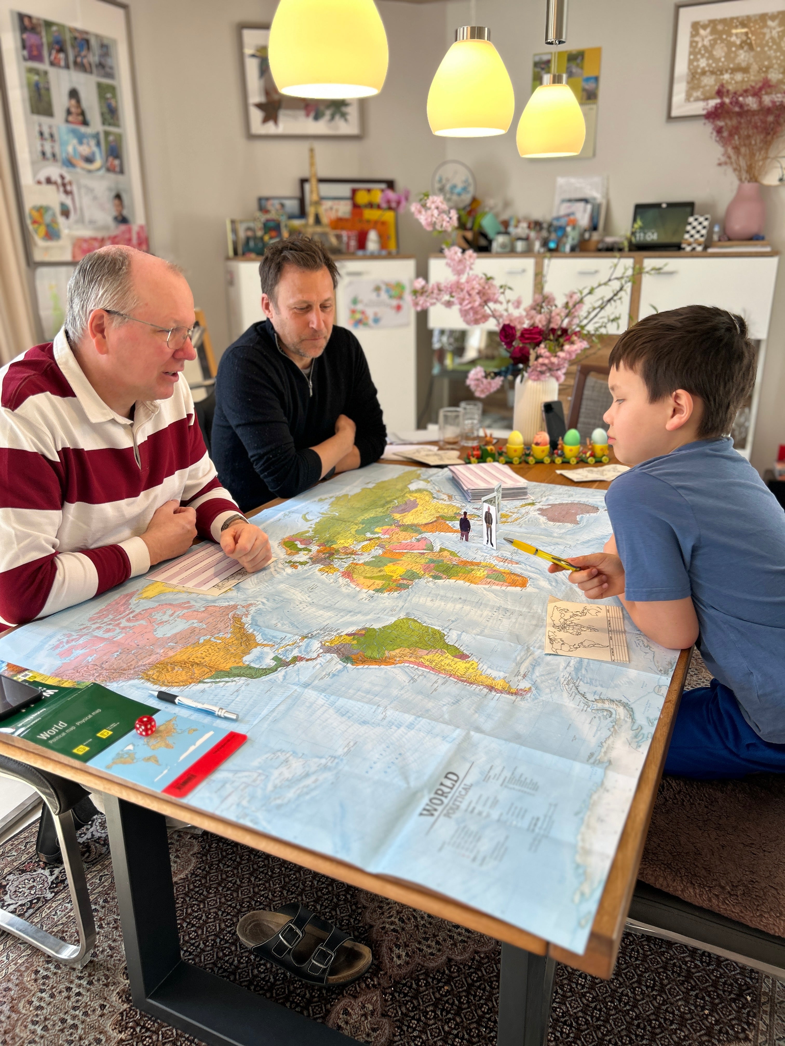 Drei Spieler sitzen um eine echte XXL-Weltkarte und spielen WELTKARTE