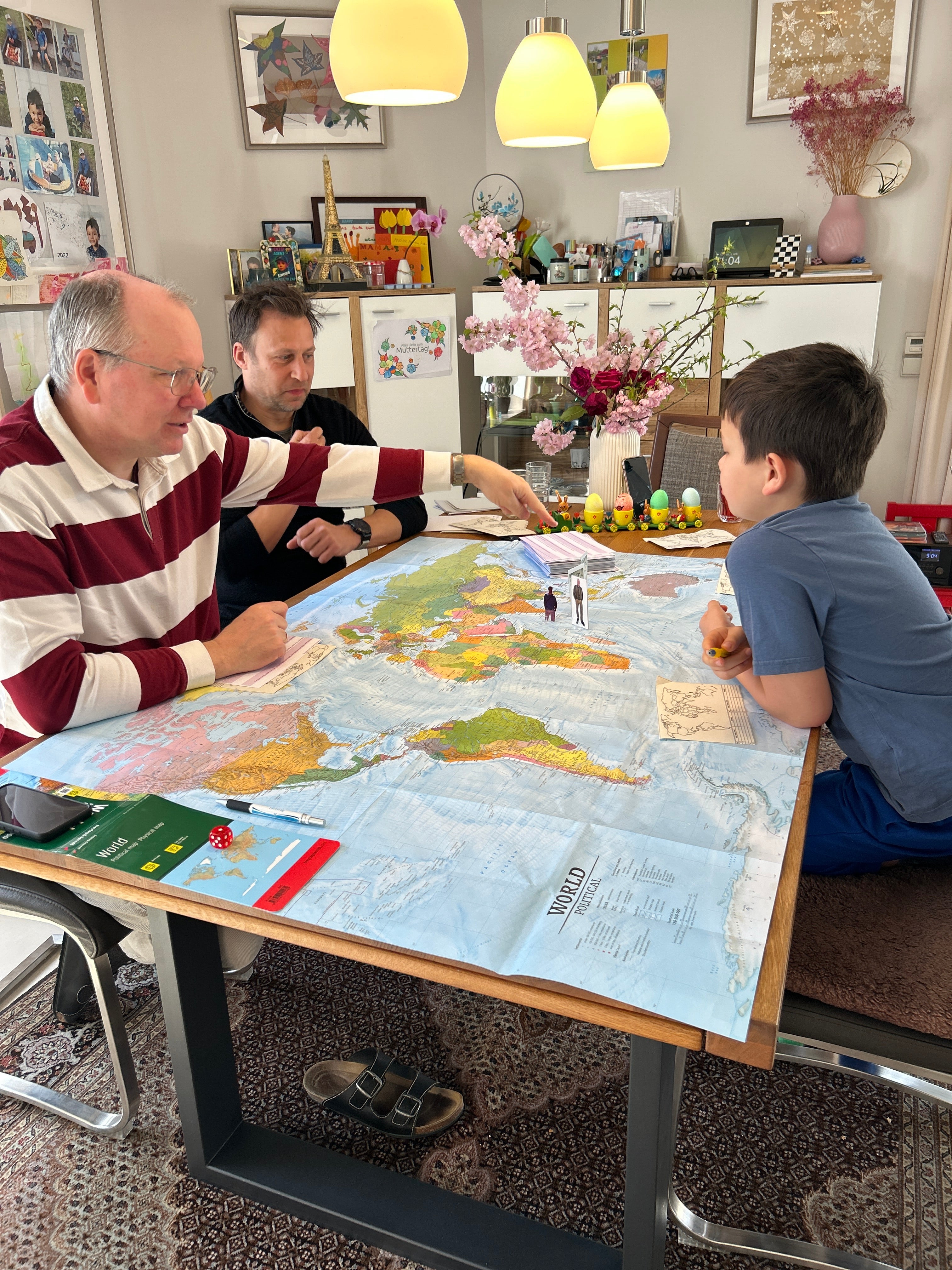 Zwei Erwachsene und ein Kind spielen das Geografie-Brettspiel WELTKARTE